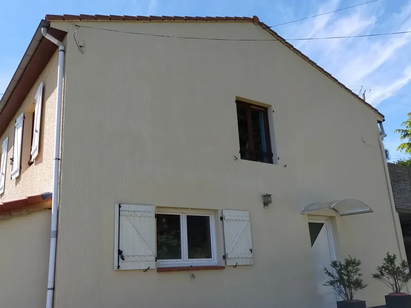 Façade repeinte en finition crème uniforme, volets et fenêtres remis en place