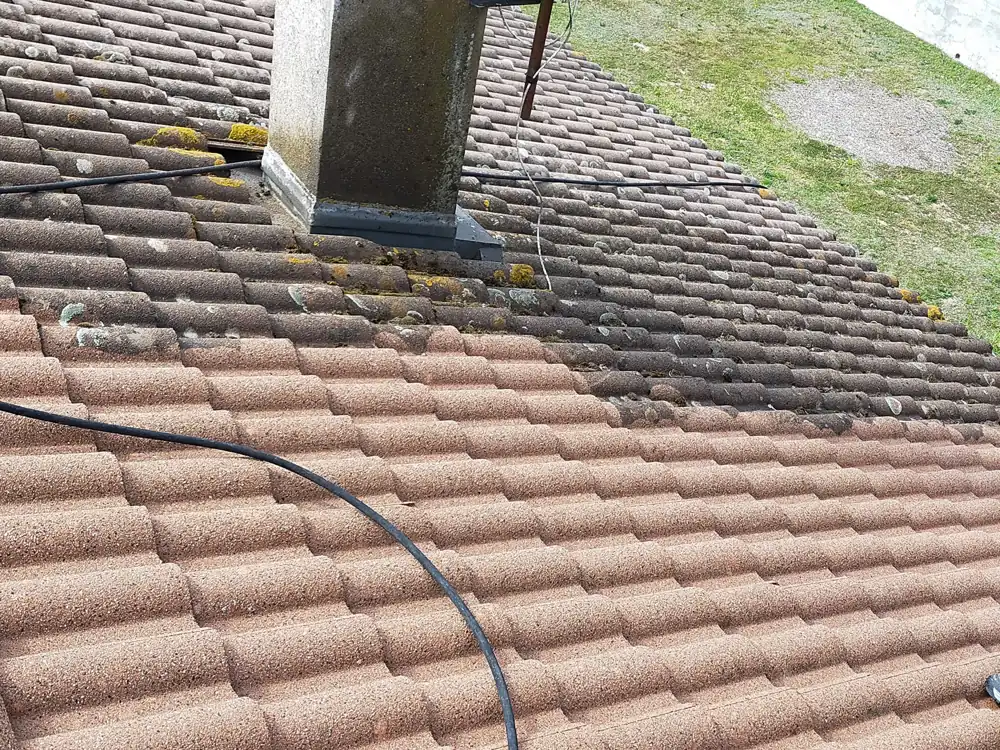 Toiture en tuiles béton pendant un démoussage : partie basse nettoyée, partie haute couverte de mousse et de lichen