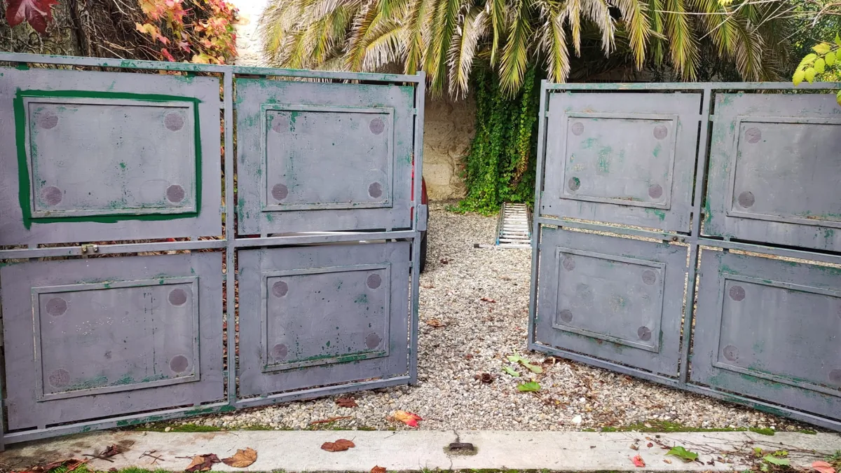Avant : portail métallique gris, taché et écaillé sur les deux vantaux
