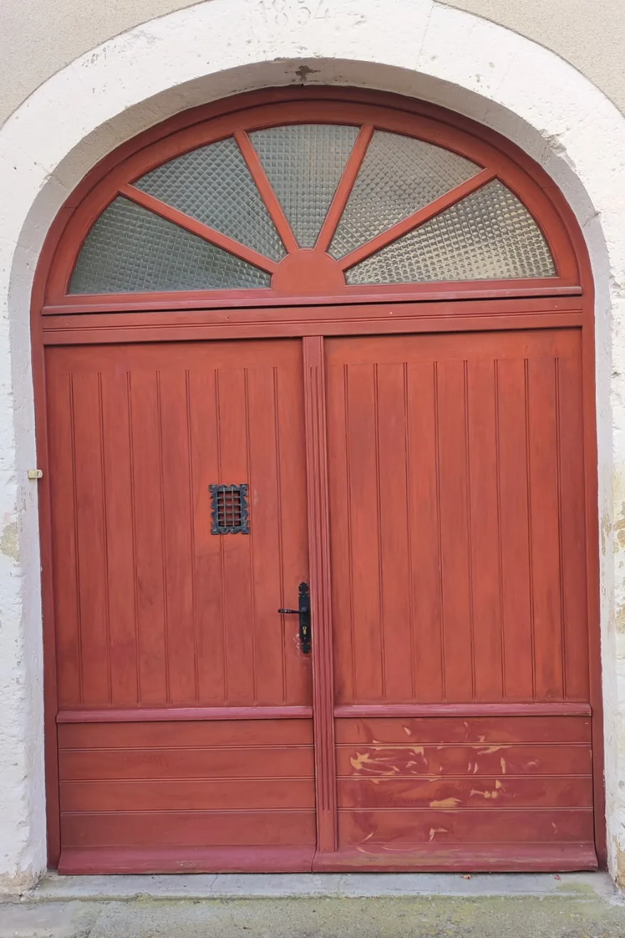 Avant : porte de garage cintrée dont la teinte rouge a passé et s'est tachée