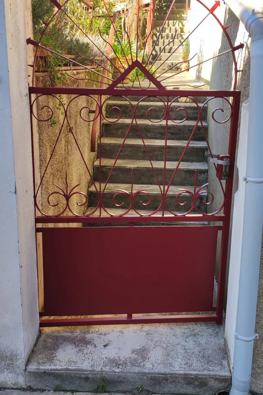 Après : portillon en fer forgé repeint en rouge, volutes et tôle basse uniformes