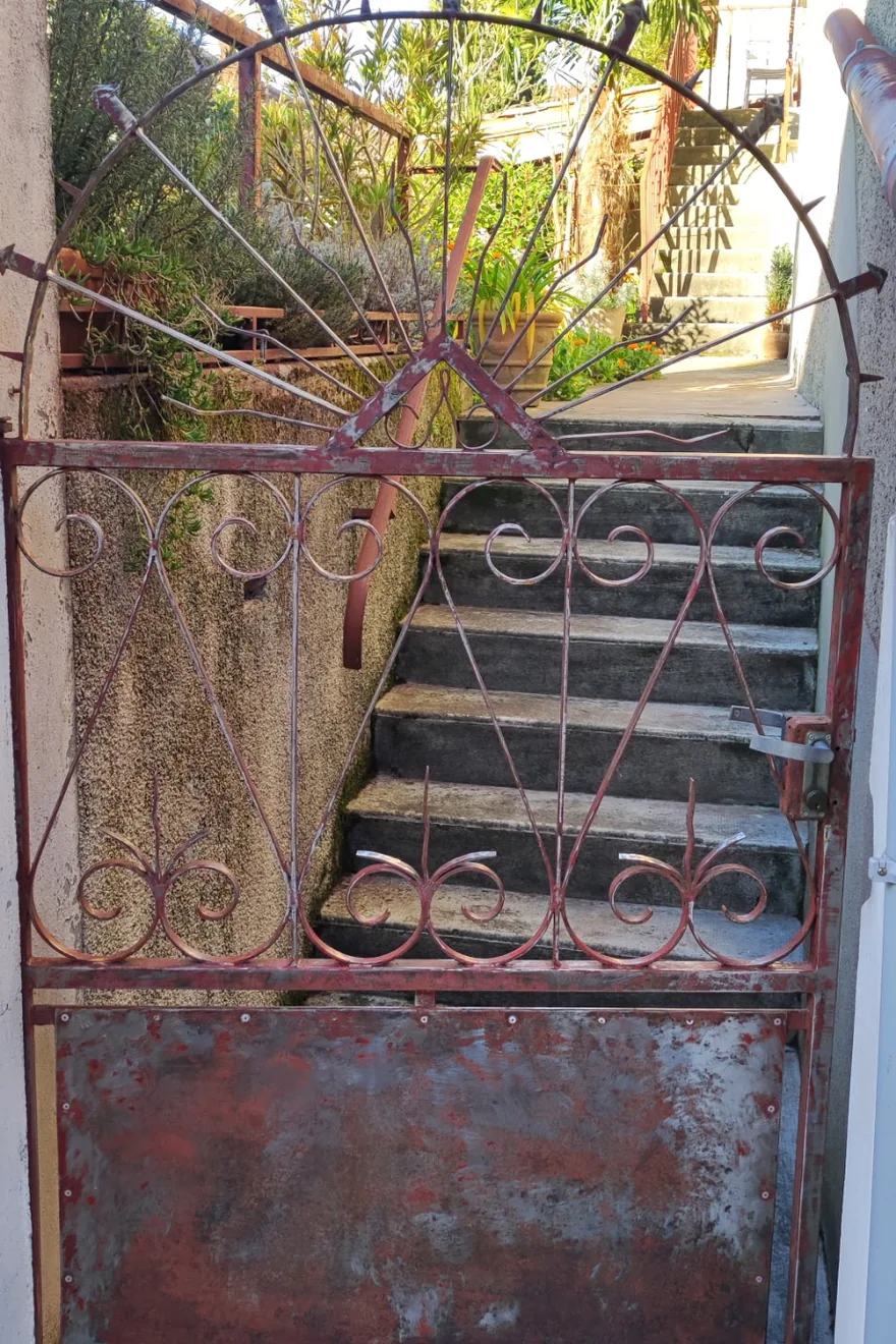 Avant : portillon en fer forgé rouillé, peinture écaillée sur les volutes et la tôle basse