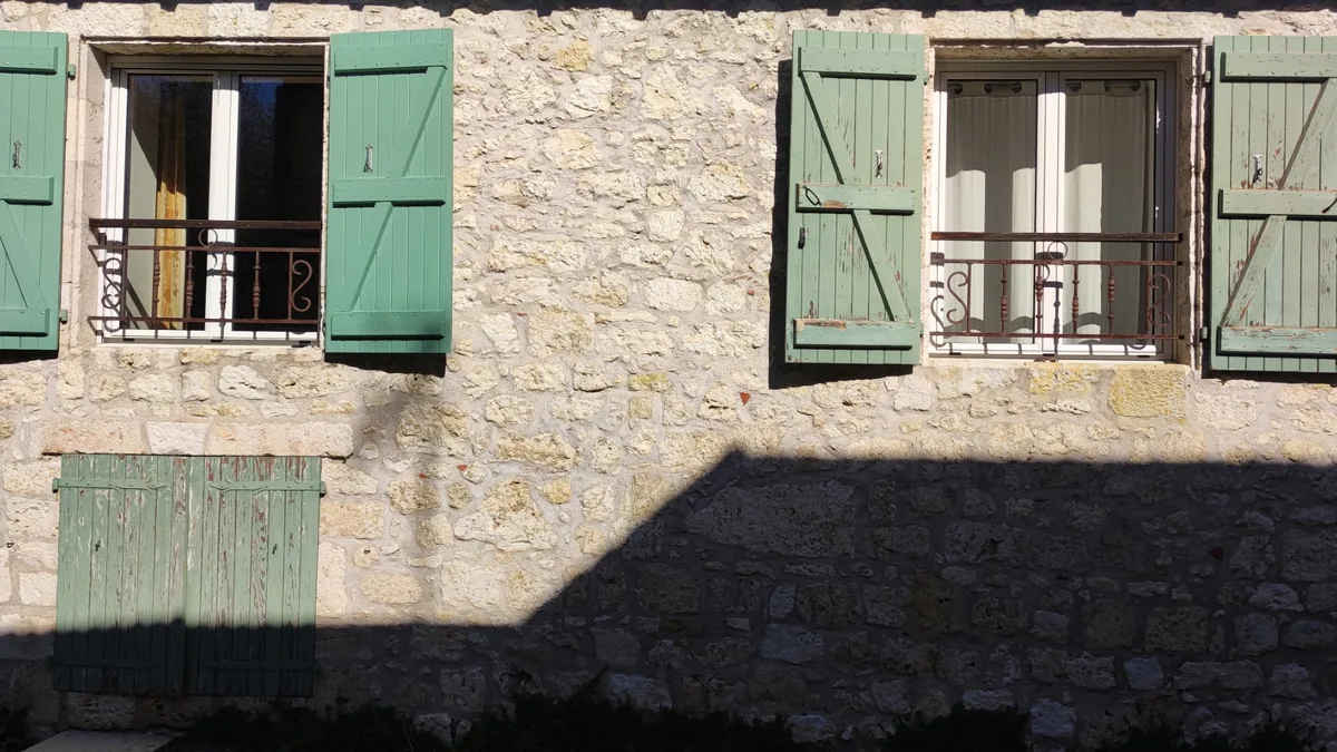 Volets en bois peints en vert d'eau sur une façade en pierre, fenêtres et soupirail